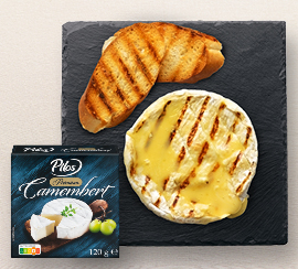 Sýr Camembert na černém talíři s 2 kousky pečiva na šedém pozadí
