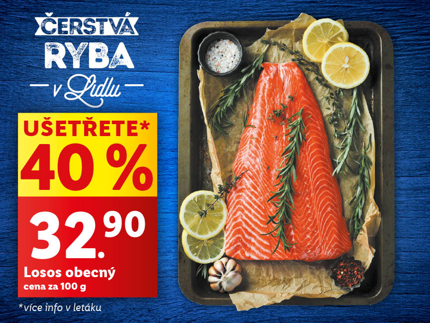 Velký kus lososa na černém talíři a tmavě modrém pozadí. Okolo lososa jsou plátky citrónu a bylinky. Cena za 100 g je 32,90 Kč se slevou 40 %.